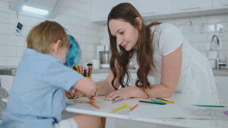Junge-Schöne-Mutter-Und-Sohn-Zeichnen-Mit-Buntstiften,-Die-Am-Tisch-In-Der-Küche-Sitzen